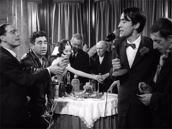 Placido (Cassen), y Quintanilla (José Luis López Vázquez) a la izquierda; al fondo el pobre antes de sentarse a cenar mientras se hace el programa de radio que cubre la campaña Siente a un pobre en su mesa. Plácido de José Luis García Berlanga. Análisis y resumen de Plácido de Berlanga. Cultugrafía, difusión y crítica cultural.