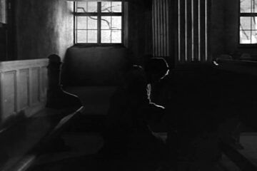 La imagen, de estilo expresionista, muestra a una mujer arrodillada, como si estuviera confesándose. Los comulgantes (1963), de Ingmar Bergman.