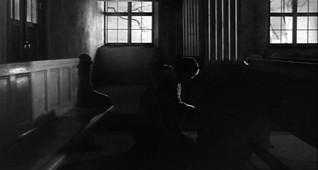 La imagen, de estilo expresionista, muestra a una mujer arrodillada, como si estuviera confesándose. Los comulgantes (1963), de Ingmar Bergman.