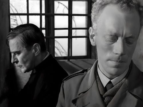 La imagen muestra a dos hombres en blanco y negro, uno vestido con sotana y el otro con un abrigo, de pie frente a una ventana. Ambos hombres parecen estar en profunda reflexión. La imagen tiene una atmósfera melancólica y evoca una sensación de soledad y aislamiento.
Película Los comulgantes de Ingmar Bergman