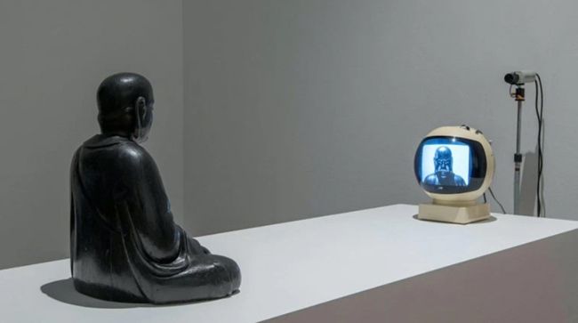 TV Buddha (1974). Nam June Paik. Obra visionaria de este artista coreano que preconizaría la alienación de la sociedad actual, dominada por un materialismo cultural donde la exhibición del ego oculta un vacío existencial tras una insaciable búsqueda de satisfacción, convirtiendo al individuo en consumidor y producto de una sedación digital desnaturalizadora.